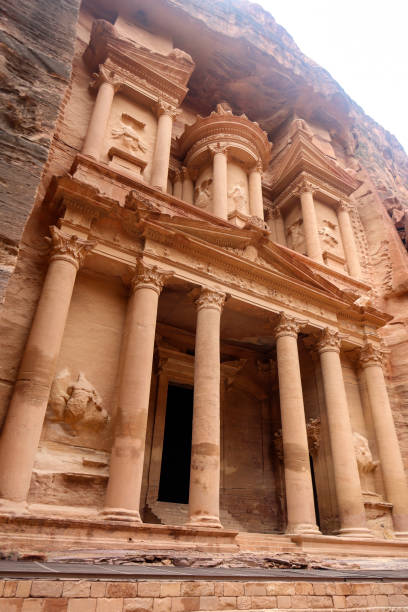 View of the Al-Khazneh Palace or Treasury in Petra, Jordan. The building is carved into a huge rock, has an elegant pediment and towering columns.