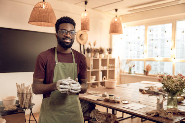istock Dark-skinned smiling sculptor with wet clay in hands looking contented 2156628369