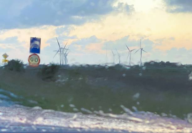 Driving through heavy rain in western Jutland, Denmark, we pass by Scandinavian windmills against the backdrop of a sunset. Denmark's weather conditions make wind power one of the most advantageous sustainable energy sources. Since the late 1970s, Denmark has developed strong technological and research expertise in wind power. By 2011, the Danish wind industry accounted for about a quarter of the global wind turbine market.
