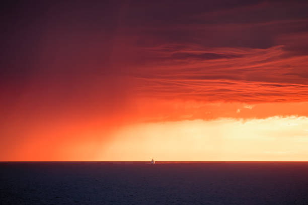 A large motor yacht passing a large storm on the horizon of the Mediterranean sea against a dramatic orange sunset