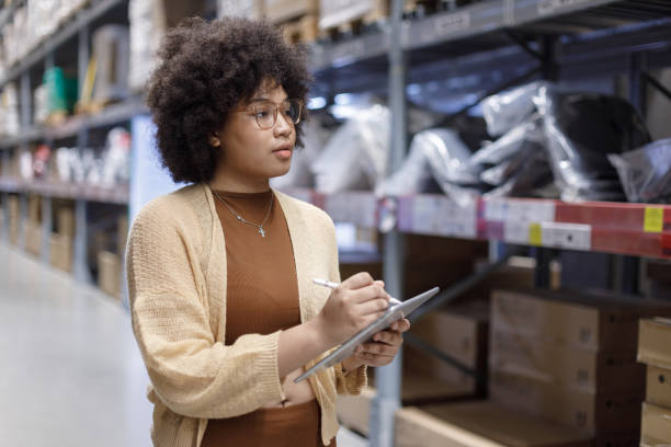istock Young African American female looking at camera working in warehouse using digital tablet checking inspection on shelves.woman worker check stock inspecting in storage logistic factory. 2156644540