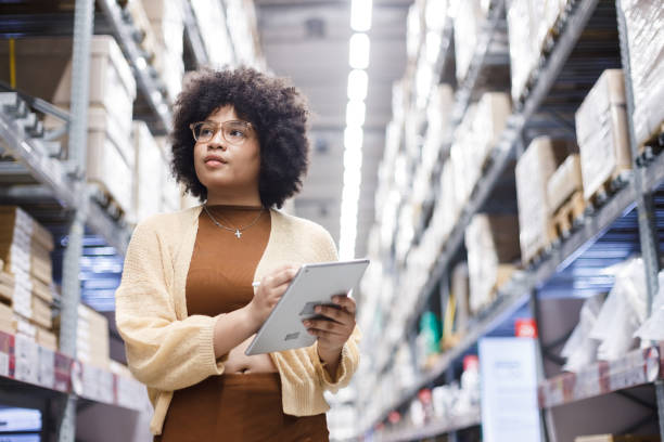 istock Young African American female  working in warehouse using digital tablet checking inspection on shelves.woman worker check stock inspecting in storage logistic factory. 2156644545