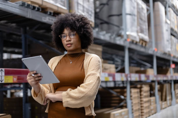 istock Young African American female looking at camera working in warehouse using digital tablet checking inspection on shelves.woman worker check stock inspecting in storage logistic factory. 2156644622