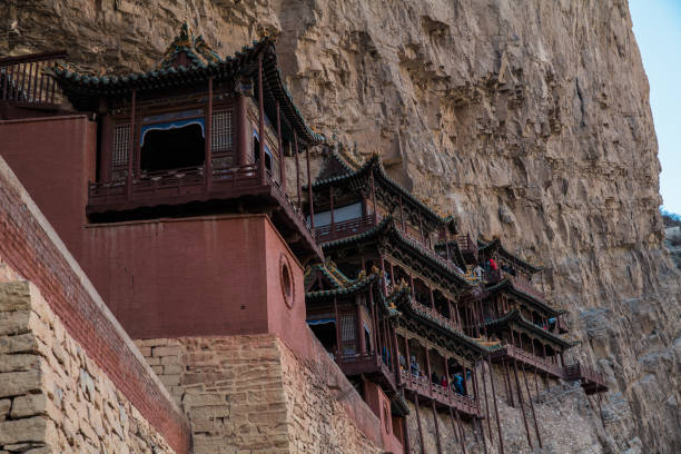 A huge statue of Buddha, carved into the rock, is surrounded by many tourists. The sunlight makes the statue look very solemn, reflecting the greatness of ancient art