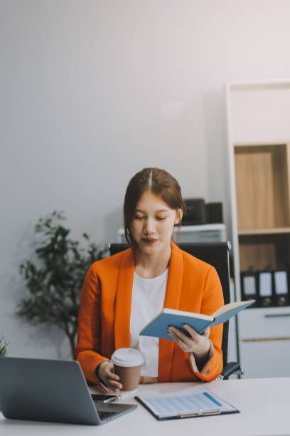 istock Beautiful smiling Asian businesswoman holding a coffee cup while taking notes at office. 2156662210