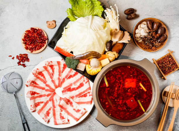 Spicy Hot Pot Set with meat slice, cabbage, baby corn, broccoli, mushroom, red chilli, chopsticks and fork served in pot isolated on background side view of taiwanese food
