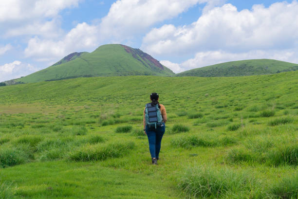 An Asian mid-adult woman using solar cell on her backpack to power her small devices during trekking in on the grassland of mountain, on the go for campsite
