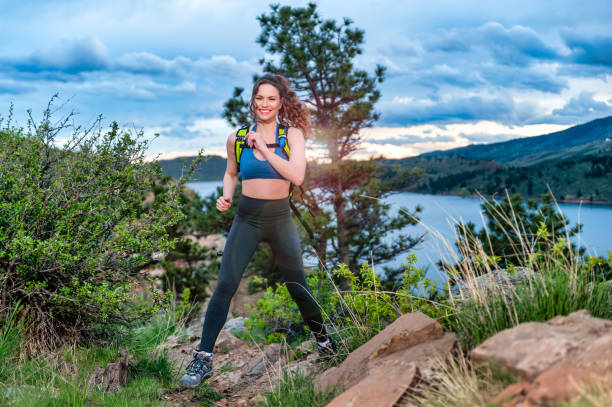 Beautiful young woman jumping on rocks with lake and snowcapped Rocky Mountains in background