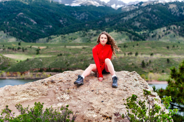 istock Young woman sitting on rocks with mountains in background 2156674898