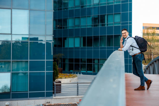 A professional businessman engages in a conversation via smart phone against a city landscape, symbolizing corporate business and success in downtown district