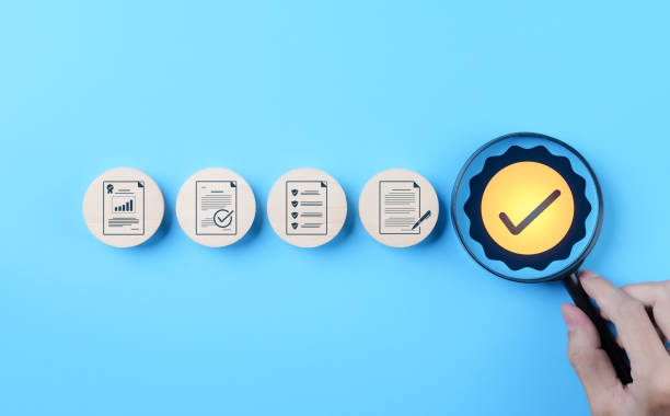 Quality Control and Certification Assurance Concept. Hand holding magnifying glass over checkmark symbol, alongside icons representing quality control, certification, and assurance on blue background.
