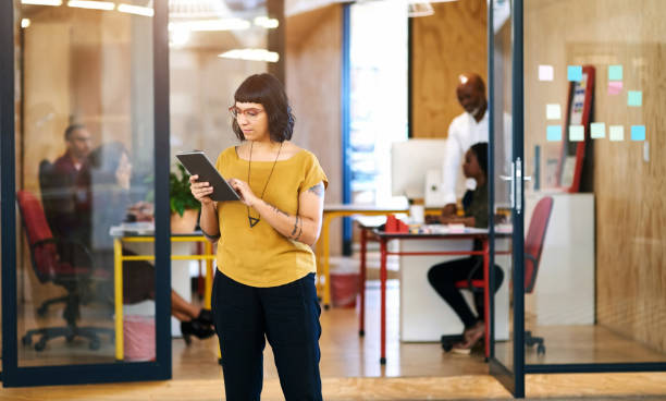 istock Woman, tablet and corridor at startup office with thinking, typing and check notification on web. Person, internship and digital touchscreen with ideas, click and reading with app at creative agency 2156678454