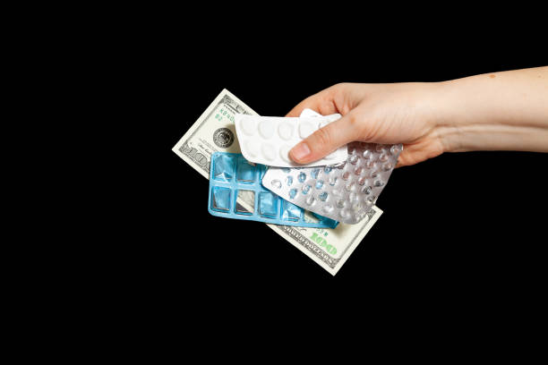 Buying drugs for dollars. One hundred dollar bill and empty pill blisters in hand on black background
