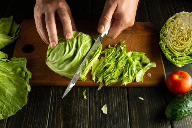 istock Chef hands with a knife while cooking on a kitchen black table. Delicious salad for breakfast with fresh vegetables by the hands of the cook 2156679221