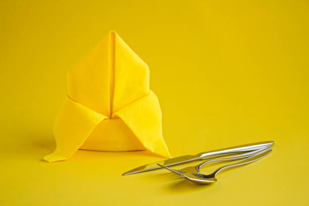 Yellow Color Paper Napkin folded in bishop's hat or lily flower on the yellow background with cutlery set and copy space.