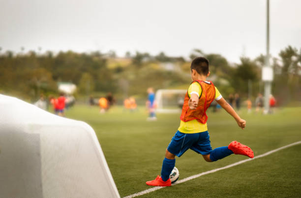Boy in sports clothing hitting or kicking soccer ball, playing football in football stadium.