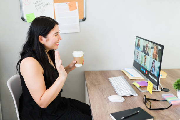 istock Professional woman engaged in an online conference call with colleagues, gesturing while holding a coffee cup in a modern office setting 2156701611
