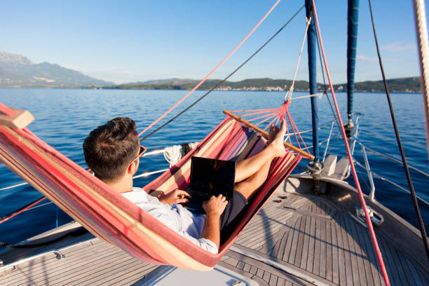 istock Working in traveling. Freelancer using laptop, Internet. Business man with computer in beach hammock. Sea summer vacation on yacht, workation lifestyle. Digital nomad workplace in nature outdoors 2156702129