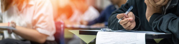 Exam at school with student's taking educational admission test in class, thinking hard, writing answer in university classroom, education and world literacy day concept