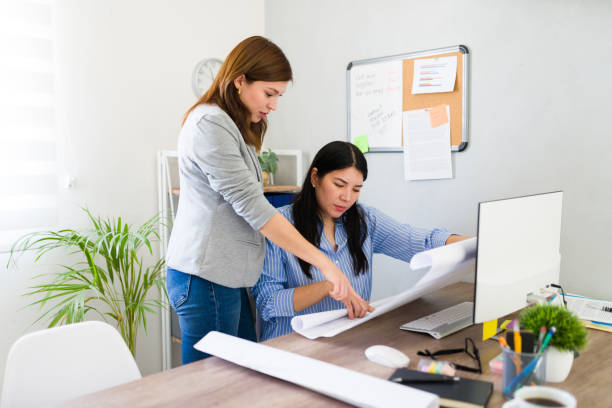 istock Two women collaborating and strategizing in a modern startup office with computer and paperwork 2156705535