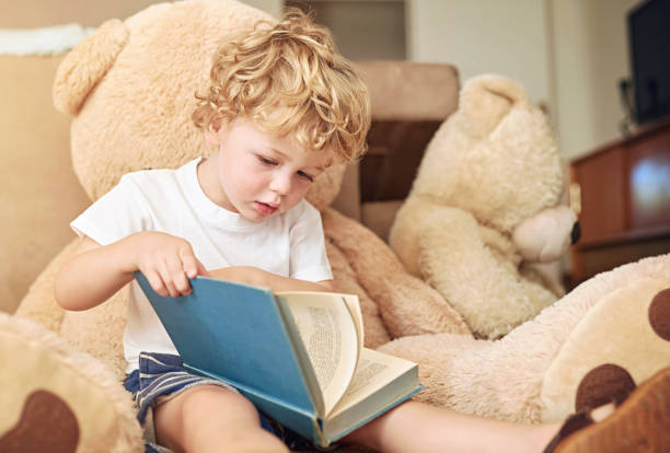 istock Boy, reading and book on sofa at house for learning literature, language development or studying of knowledge. Child, relax and information with novel, fantasy story or activity for education growth 2156709650