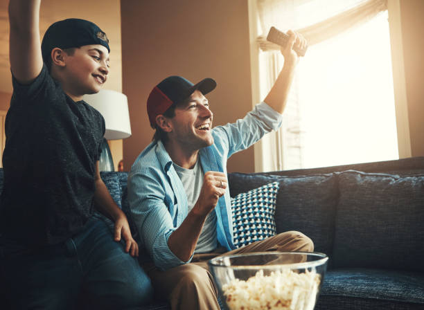 istock Tv remote, popcorn and man with kid in celebration for network, subscription and bonding at home. Dad, son and happy with fist in success for sports, winning and watching live broadcast together 2156718178