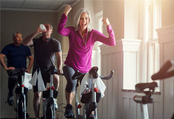 Fitness, cycling and happy woman in gym for celebration, achievement and goal victory. class, senior people and female athlete as winner, training and exercise success with workout machine Reaching my goals one class at a time man 60s bicycle stock pictures, royalty-free photos & images