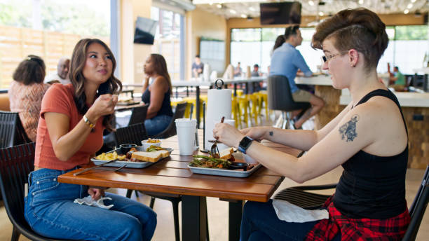 istock Two Friends Chatting inside BBQ Restaurant with Patrons in Background 2156725591