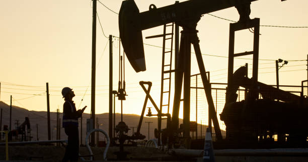 An Indian oilfield worker facing an oil pump jack at sunset in Kern County, California.