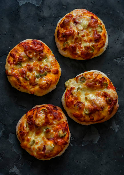 istock Mini pizza with ham, olives and mozzarella - a delicious snack, tapas on a dark background, top view 2156734825