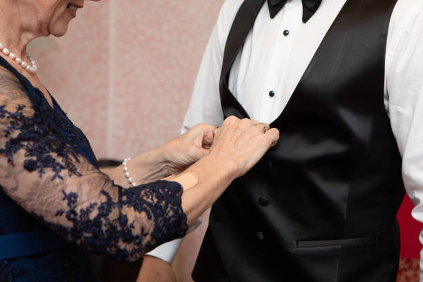 Elegant mother helping son buttoning up vest on wedding day