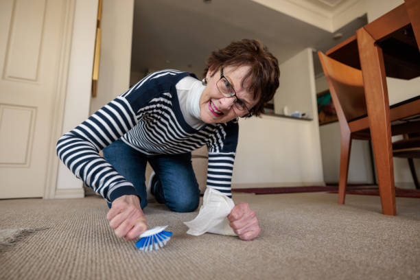 Janitor wearing orange gloves diligently cleaning the floor with a microfiber mop in a cozy living room, ensuring hygiene and cleanliness