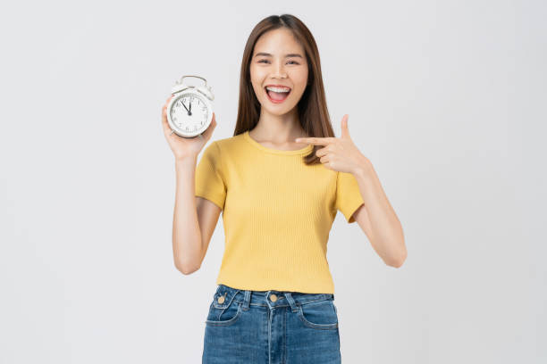 istock Young asian woman holding alarm clock and smiling isolated on white background studio. 2156754190