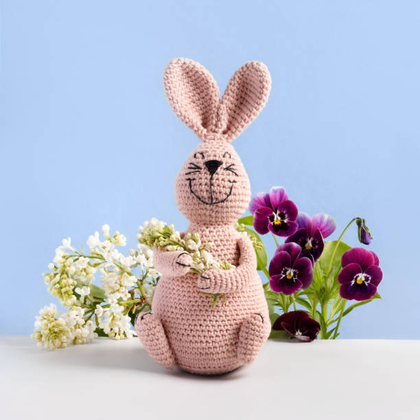 Knitted toy pink bunny with white lilac and bouquet of spring flowers of lilac and viola on blue background. Concept of spring, Easter, Mother's Day