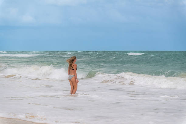 Cancun, Quintana Roo, Mexico, December 14, 2023: Young woman considering whether to enter a raging sea during red flag signal
