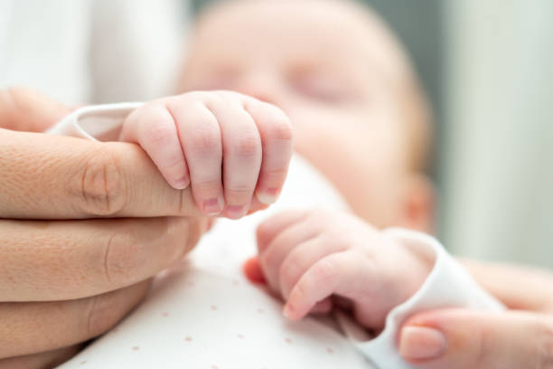 istock Mother's hand cradled by baby's tiny fingers. Concept of unconditional love from first touch 2156768934