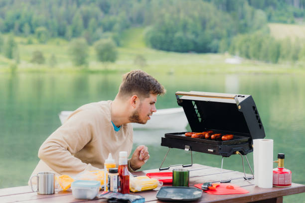 istock Man Grilling Sausages With Scenic Lake View 2156777037