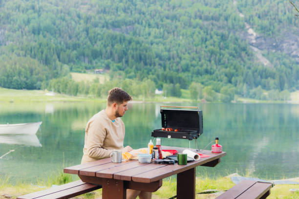istock Man Grilling Sausages With Scenic Lake View 2156777680