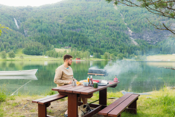 istock Man Grilling Sausages With Scenic Lake View 2156778570