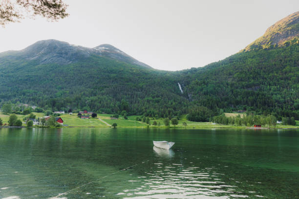 Scenic View of beautiful mountain village with white boat by the lakeshore with green mountains and waterfall view in Jostedalbreen National park, Western Norway, Scandinavia