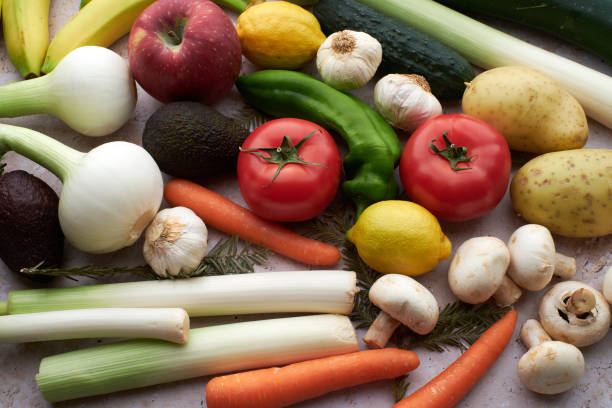 A vibrant arrangement of fresh produce including a red apple, tomatoes, leeks, and other vegetables.