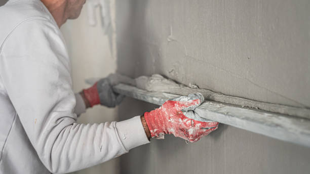 istock Machine plastering. Applying gypsum plaster by mechanized method on a wall. A worker hand removes excess plaster with leveler. 2156794967