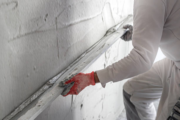 istock Machine plastering. Applying gypsum plaster by mechanized method on a wall. A worker hand removes excess plaster with leveler. 2156795163