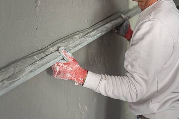 istock Machine plastering. Applying gypsum plaster by mechanized method on a wall. A worker hand removes excess plaster with leveler. 2156795164
