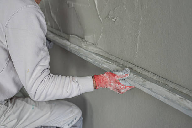 istock Machine plastering. Applying gypsum plaster by mechanized method on a wall. A worker hand removes excess plaster with leveler. 2156795181