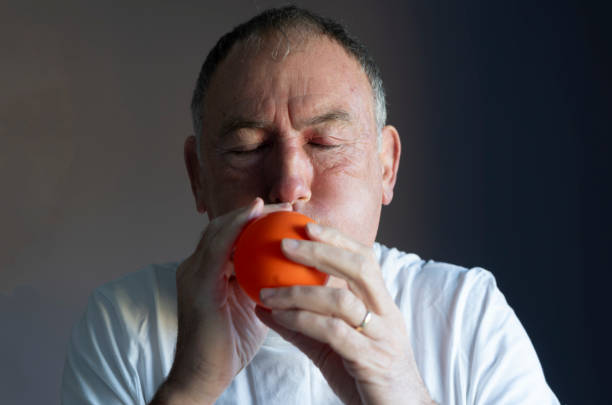 Senior man blowing up an orange balloon.