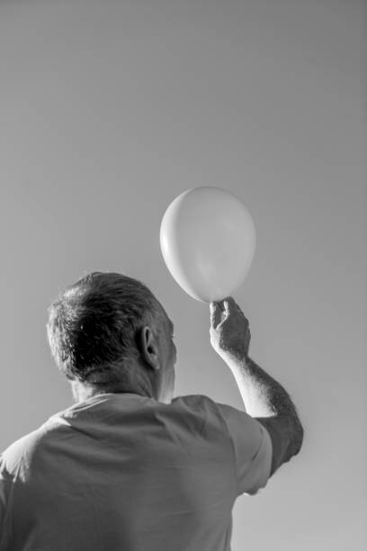 Senior man holding up a balloon against a clear sky.