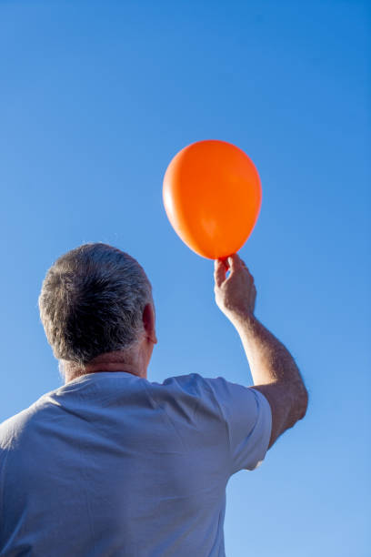istock Senior man holding up an orange balloon 2156799125