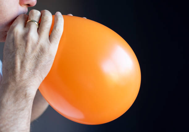 Senior man blowing up an orange balloon.