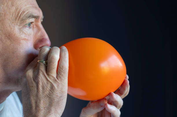Yellow water filled balloon hitting on man's face against black background.